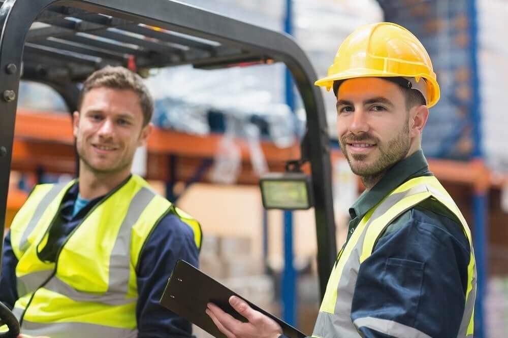 Ein Arbeiter im Gabelstapler, ein anderer stehend davor