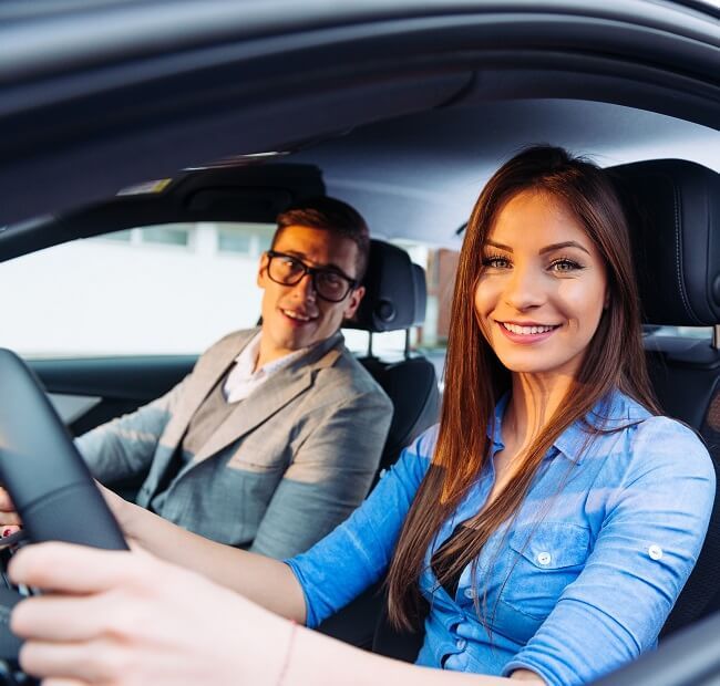 Lachende Fahrschülerin mit Fahrlehrer im Auto